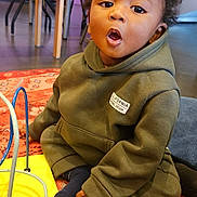 Zayonn participe au concours pour gagner de l'argent avec cette photo : background, carpet, casual_clothing, child, colorful, curious, curly_hair, expression, floor, furniture, home, hoodie, indoor, person, play_area, seated, socks, toddler, toy, young_child