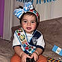 Nashly is registered to the contest to win money with this photo: toddler, child, remote_control, headband, bow, embroidered_sash, toy_xylophone, flag, guatemala, blanket, orange_pants, white_shirt, smiling, indoors, furniture, face, hands, happy, colorful, young_child