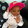 baby, child, infant, smiling, happy, portrait, pink_hat, cap, floral_outfit, onesie, sitting, couch, indoor, face, eyes, hands, earring, patterned_fabric, family_photo, close_up