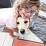 Aria a rejoint le concours — aidez-le/la à gagner de superbes lots ! child, dog, glasses, smiling, hug, indoor, barefoot, rug, blanket, tile_floor, happy, pet, friendship, playful, casual_clothing, light_hair, young, affection, cute, portrait