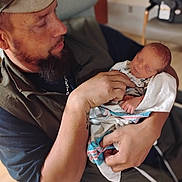 Wyatt joined the competition — help win amazing prizes! man, baby, newborn, holding, hospital_blanket, beard, cap, indoor, person, sleeping, care, love, family, portrait, hands, face, clothing, chair, tattoo, gentle
