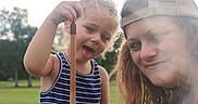 River Grace is registered to the contest to win money with this photo: child, person, outdoor, grass, stick, cap, striped_clothing, smile, tongue_out, fun, young, casual, nature, daytime, two_people, portrait, happy, playful, summer, field