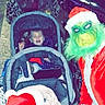 River Grace joined the competition — help win amazing prizes! child, children, stroller, winter_clothing, hat, santa_hat, grinch_costume, person, outdoor, nighttime, holiday, christmas, costume, smile, festive, urban, people, jacket, face, celebration