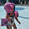 child, pool, water, floaties, pink_hat, swimsuit, outdoor, summer, sunlight, recreation, swimming, playing, water_toys, fun, daytime, vacation, kid, safety, leisure, holiday