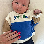 Théo a rejoint le concours — aidez-le/la à gagner de superbes lots ! baby, infant, sweater, clothing, hand, nail_polish, pink_nails, person, face, skin, eyes, fingers, fabric, button, blue_clothing, beige_clothing, white_background, portrait, cute, indoor