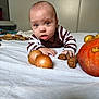 baby, infant, bed, onion, walnut, pumpkin, striped_clothing, curious, indoor, white_bed_sheet, child, face, hands, person, food, vegetables, fruit, orange, brown, closeup