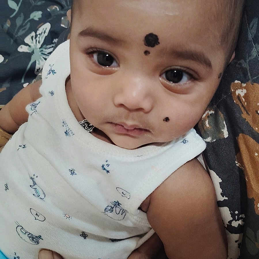 Yashvin is registered to the contest to win money with this photo: baby, black_dot, child, closeup, clothing, cushion, cute, expression, eyes, face, hand, holding, indoor, infant, patterned_fabric, person, portrait, resting, skin, sleeveless_top