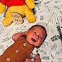 baby, newborn, smiling, plush_toy, winnie_the_pooh, blanket, leaf_pattern, brown_outfit, buttoned_clothing, infant, happy, lying_down, cute, child, soft_toy, indoor, portrait, small_child, toddler, cozy