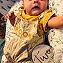 Westin is registered to the contest to win money with this photo: baby, infant, two_months, overalls, yellow_shirt, pooh, milestone_sign, cushion, leaf_pattern, footwear, sneakers, curious_expression, lying_down, indoors, close_up, child, cute, portrait, small_hands, soft_lighting