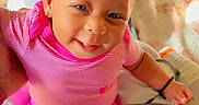 Iyla is registered to the contest to win money with this photo: baby, bed, bedding, bracelet, child, cozy, earrings, eyes, face, hair, happy, indoor, infant, pants, pink_clothing, portrait, sitting, smiling, socks, striped_shirt