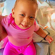 Iyla is registered to the contest to win money with this photo: baby, bed, bedroom, blanket, child, cozy, eyes, face, happy, indoor, infant, jewelry, pants, pillows, pink_clothing, portrait, sitting, smiling, socks, striped_shirt