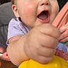 Paisley is registered to the contest to win money with this photo: baby, child, blue_eyes, hand, toy, yellow_toy, happy, expression, close_up, face, skin, mouth_open, fingers, clothing, purple_shirt, indoor, person, infant, joy, playtime