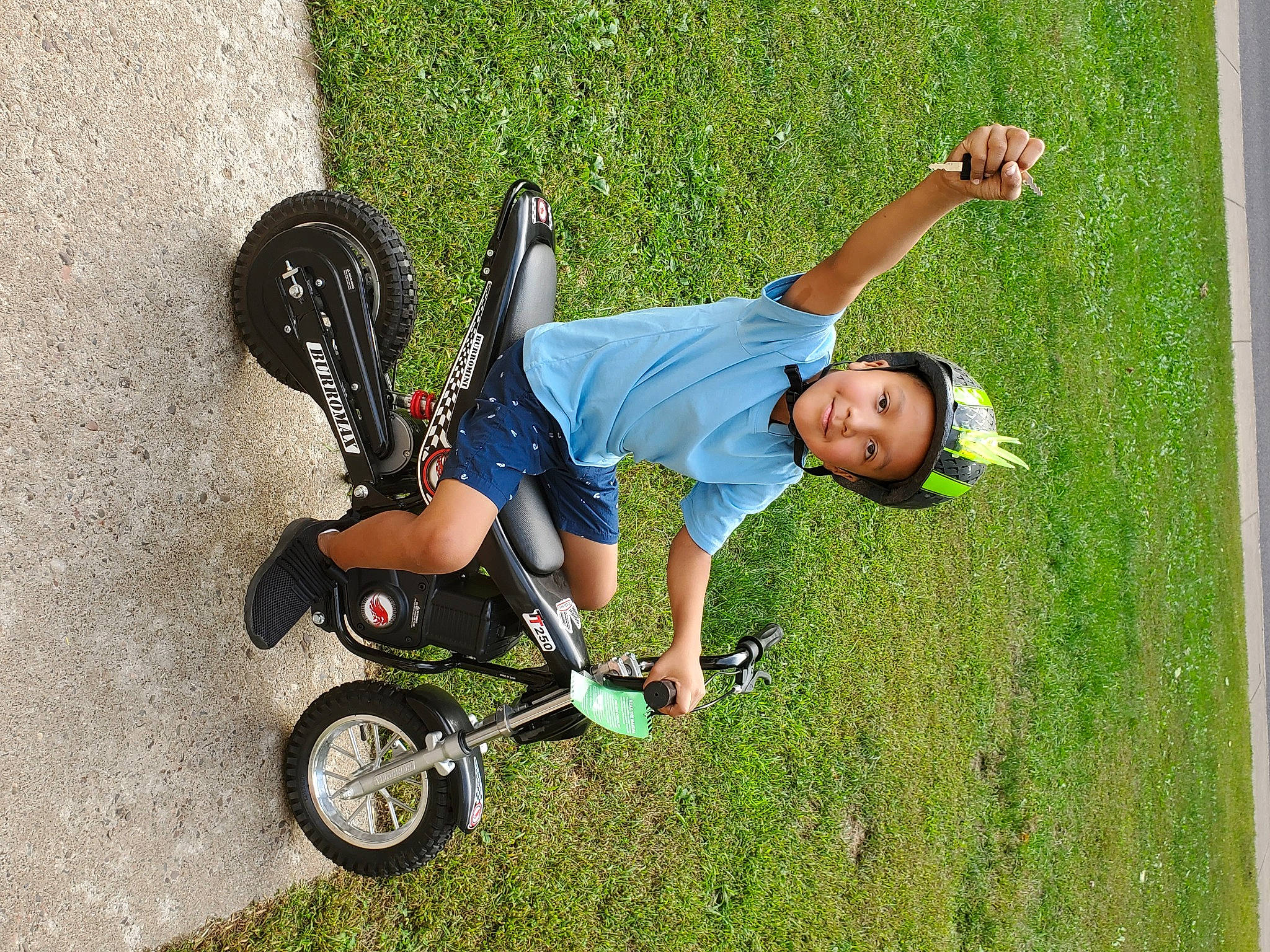 Maurice is registered to the contest to win money with this photo: automotive_tire, bicycle_tire, fun, grass, grassland, happy, headwear, joy, knee, lawn, leisure, outdoor_recreation, people_in_nature, person, product, recreation, rolling, smile, tire, toddler