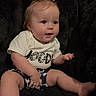 baby, child, toddler, portrait, sitting, indoors, chair, blanket, fluffy, black_background, ponytails, blonde_hair, blue_eyes, wide_eyed, smiling, graphic_shirt, shorts, barefoot, cute, photography