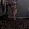 Ellie joined the competition — help win amazing prizes! baby, child, toddler, standing, pacifier, crib, nursery, indoor, carpet, home, portrait, candid, dim_lighting, pink_clothing, short_hair, looking_at_camera, furniture, wall, exploring, early_walker