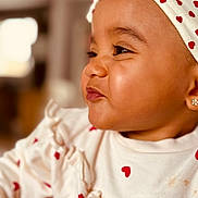 Siyanna a rejoint le concours — aidez-le/la à gagner de superbes lots ! baby, child, close_up, face, headband, earrings, white_clothing, red_hearts, smiling, profile, cute, infant, portrait, indoor, soft_light, adorable, young_child, expression, fashion, person