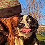dog, person, hat, blue_eyes, tongue_out, kiss, outdoor, sunlight, winter_clothing, tree, sky, park, collar, leash, black_and_white, affection, close_up, happy, pet, nature