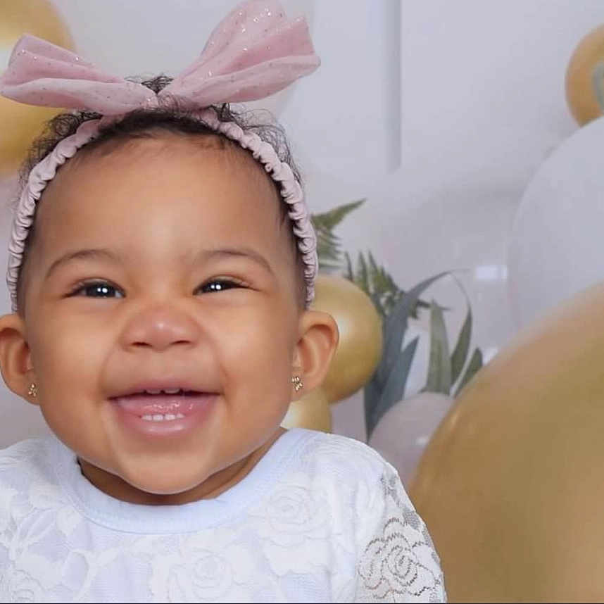 Julez is registered to the contest to win money with this photo: baby, balloons, celebration, child, closeup, cute, decorations, earrings, face, festive, girl, gold_balloons, happy, headband, indoor, joy, pink_bow, portrait, smiling, white_dress