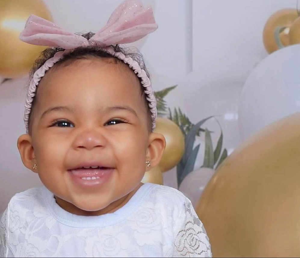 Julez is registered to the contest to win money with this photo: baby, smiling, girl, headband, pink_bow, white_dress, balloons, gold_balloons, celebration, portrait, happy, cute, closeup, child, earrings, indoor, festive, decorations, face, joy