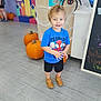 Kash joined the competition — help win amazing prizes! toddler, child, indoor, pumpkins, halloween, spider, spider_web, blue_shirt, shorts, brown_shoes, floor, balloons, chalkboard, person, smiling, hair_spike, decoration, event, colorful, background