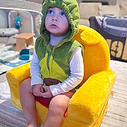 Kash joined the competition — help win amazing prizes! toddler, child, plush_chair, green_hoodie, dinosaur_costume, blue_eyes, indoor, carpet, toy, furniture, living_room, soft_lighting, cute, sitting, barefoot, expression, young_child, casual, portrait, cozy