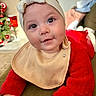 baby, headband, bib, red_clothing, fuzzy_sweater, couch, indoor, christmas_tree, decorations, holiday, face, hands, curious, child, young, portrait, smiling, cozy, festive, home