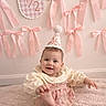 baby, infant, smiling, party_hat, pink_ribbons, half_birthday, carpet, celebration, cute, child, decorations, wall, soft_texture, happy, sitting, playful, indoors, face, clothing, portrait