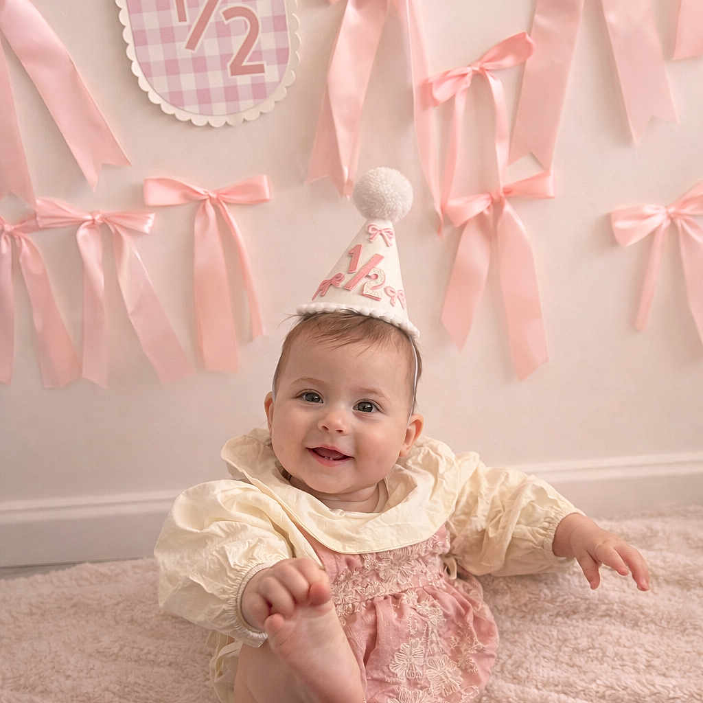 Rose participe au concours pour gagner de l'argent avec cette photo : baby, infant, smiling, party_hat, pink_ribbons, half_birthday, carpet, celebration, cute, child, decorations, wall, soft_texture, happy, sitting, playful, indoors, face, clothing, portrait