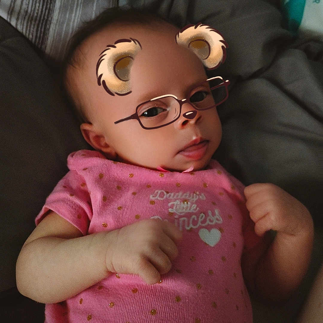 Charlotte Young is registered to the contest to win money with this photo: baby, bear_ears, bed, blanket, child, cozy, cute, expression, face_filter, glasses_filter, hand, indoors, infant, lying_down, person, pink_clothing, portrait, skin, soft_lighting, text_on_clothing