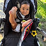 baby, child, stroller, smile, happy, outdoor, toy, playful, infant, seat, black, clothing, grass, sunlight, cute, person, legs, foot, closeup, daylight