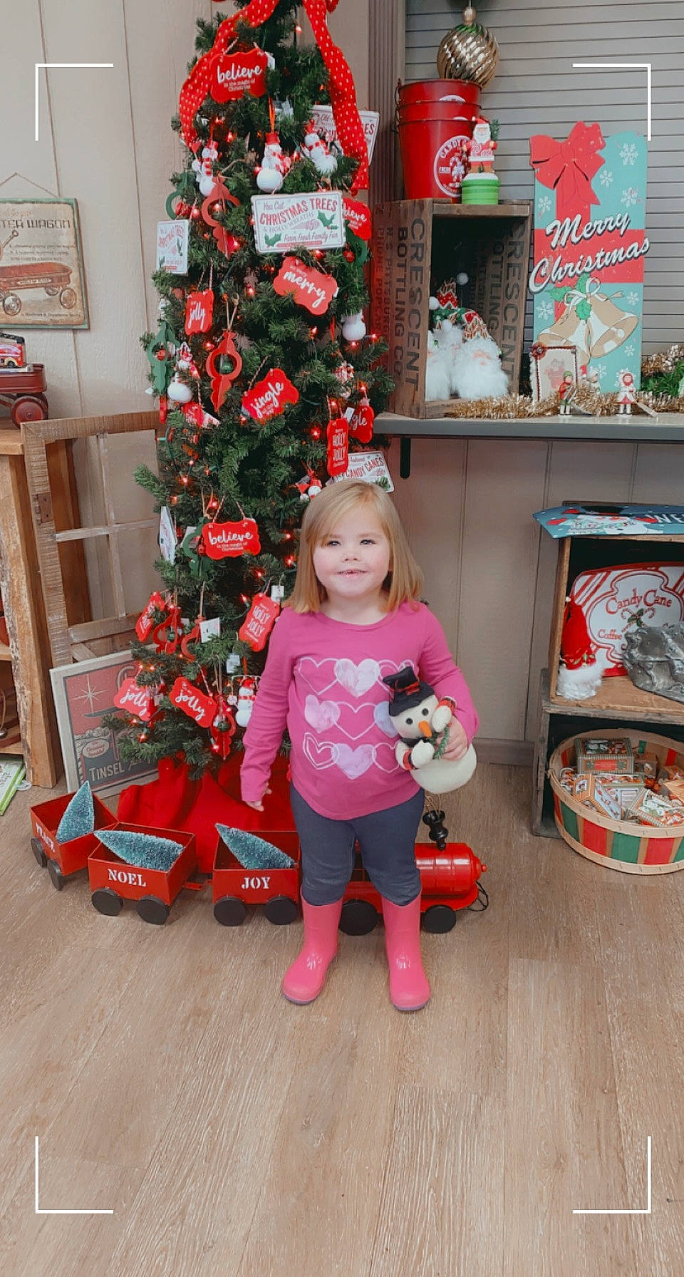 Blakely is registered to the contest to win money with this photo: baby_toddler_clothing, child, christmas_decoration, christmas_ornament, christmas_tree, event, flooring, holiday, joy, lap, magenta, ornament, person, pink, red, room, shelf, shelving, standing, toddler