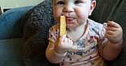 Elizabeth is registered to the contest to win money with this photo: baby, child, snack, couch, blue_couch, crumbs, face, hair, sitting, eating, hand, mouth, curious, clothing, onesie, indoor, furniture, cute, portrait, person