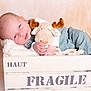 baby, infant, plush_toy, moose, crate, wooden_crate, fragile_label, blanket, soft_texture, cute, sleepy, cozy, child, portrait, indoors, comfort, small_hands, clothing, resting, peaceful