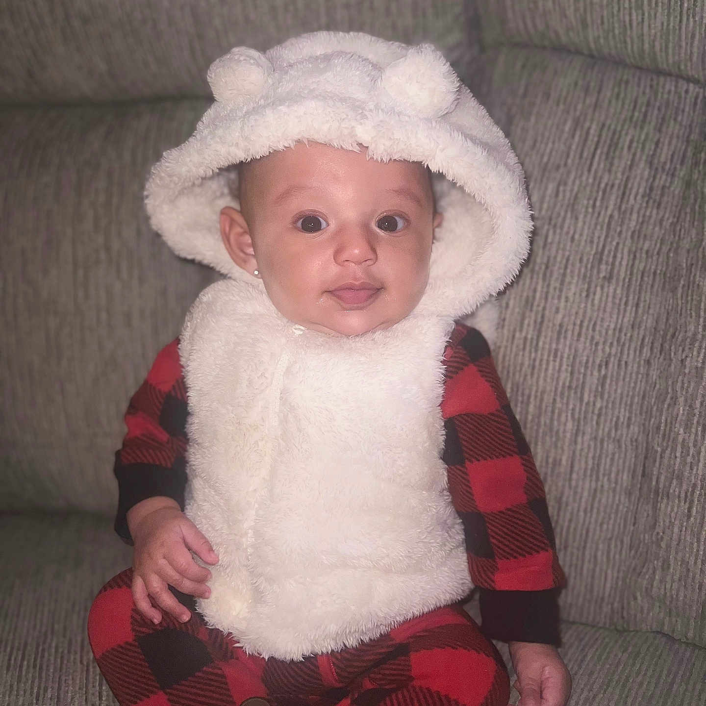 Yumi is registered to the contest to win money with this photo: baby, child, clothing, comfortable, couch, cozy, cute, ears, face, fluffy, hood, indoor, infant, person, plush, portrait, red_checkered_pajamas, seated, smiling, vest