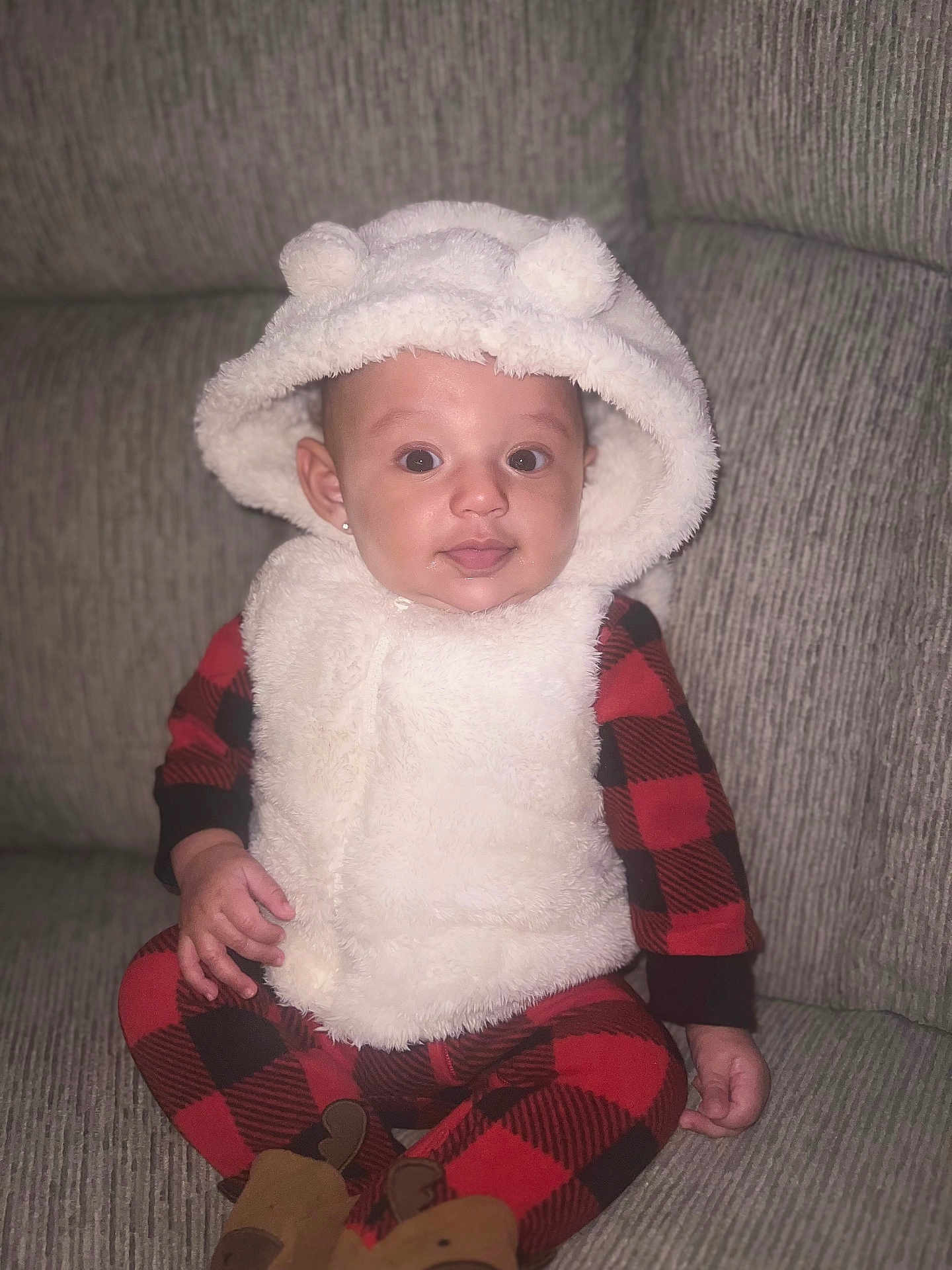 Yumi is registered to the contest to win money with this photo: baby, child, hood, fluffy, vest, red_checkered_pajamas, couch, seated, indoor, cute, smiling, face, ears, cozy, clothing, person, infant, plush, comfortable, portrait