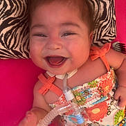 Kathryn Joy joined the competition — help win amazing prizes! baby, infant, smiling, laughing, face, orange_bow, zebra_print_pillow, floral_dress, pink_background, hand, closeup, portrait, medical_tube, tracheostomy_tube, happy, cute, fabric, bed, eye_makeup, cheeks
