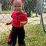 toddler, child, smile, red_bow, red_shirt, black_pants, ribbons, hair_beads, outdoor, grass, chain_link_fence, sunny_day, sidewalk, trees, happy, person, portrait, fashion, cute, playful
