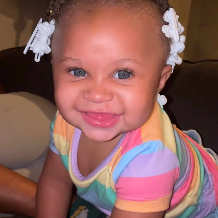 Emoni is registered to the contest to win money with this photo: toddler, child, smiling, blue_eyes, pigtails, hair_bows, colorful_clothing, striped_shirt, denim_shorts, indoor, living_room, lamp, couch, happy, portrait, cute, baby, playful, person, music_overlay