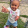 Emoni is registered to the contest to win money with this photo: toddler, child, grass, fence, colorful_hair, hair_bows, denim_shorts, tshirt, shoes, pointing, outdoor, smiling, standing, playful, chain_link_fence, sidewalk, street, person, cute, happy
