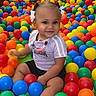 toddler, child, ball_pit, colorful_balls, indoor_playground, happy, smiling, hair_bows, shorts, tshirt, play_area, plastic_balls, seated, bright_colors, fun, playtime, person, young_child, cute, leisure