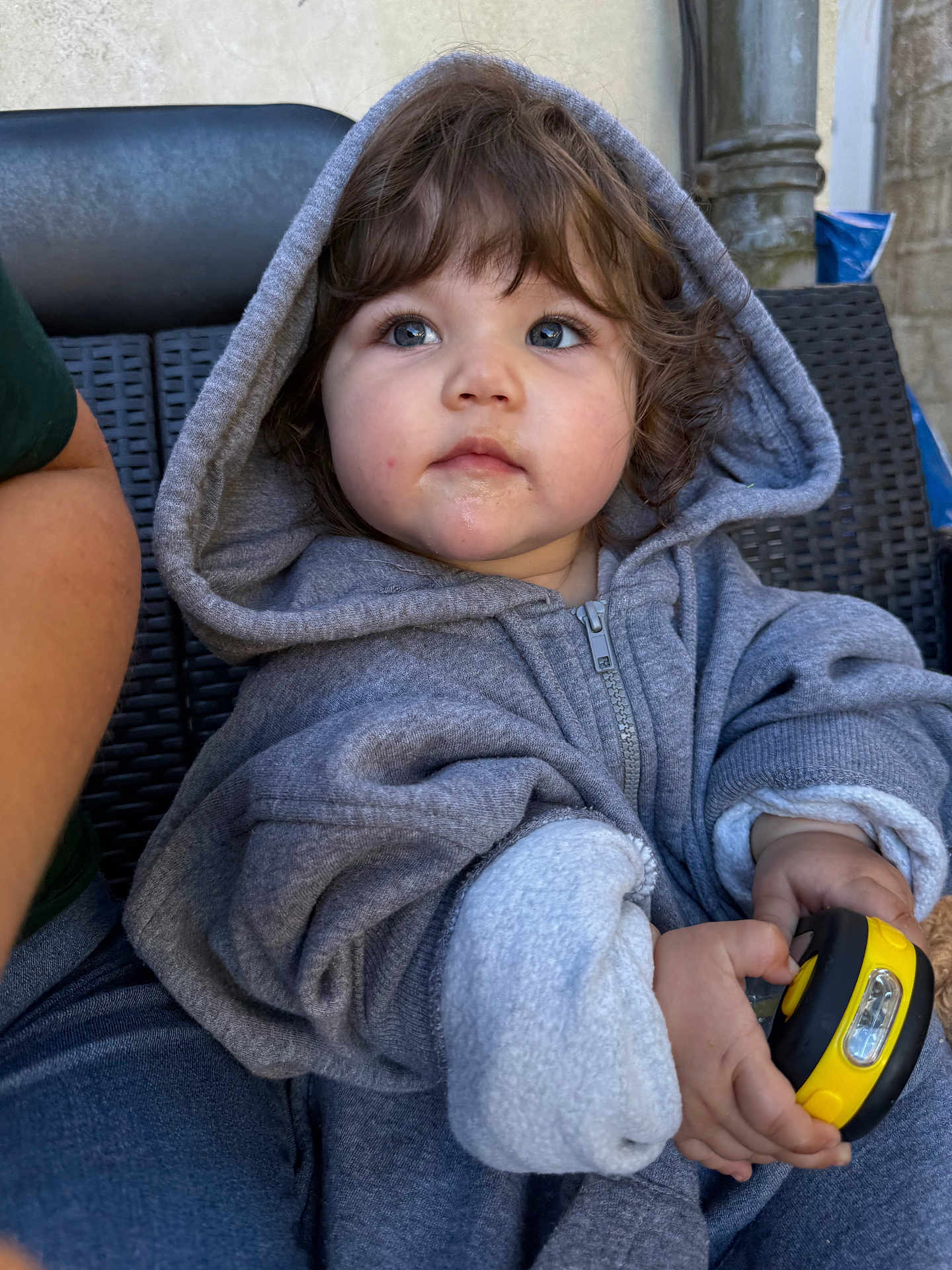 Athéna a rejoint le concours — aidez-le/la à gagner de superbes lots ! toddler, child, hoodie, gray_clothing, curly_hair, blue_eyes, handheld_object, yellow_object, outdoor, woven_chair, seated, casual_clothing, cute, curious, portrait, baby, person, cozy, young_child, closeup