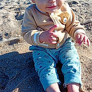 Mayron a rejoint le concours — aidez-le/la à gagner de superbes lots ! toddler, child, beach, sand, sunlight, jacket, pants, barefoot, cute, outdoor, playful, casual_clothing, smiling, young_child, daytime, small_hands, sitting, curious, sunny, nature
