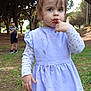 child, girl, boy, outdoor, park, trees, grass, dress, long_sleeve, finger_in_mouth, curious_expression, casual_clothing, nature, daylight, playing, childhood, messy_face, standing, young, people