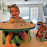 baby, infant, headband, bow, seat, toy, foot, child, happy, indoor, living_room, table, green, colorful, blurred_background, smile, person, cute, play, home