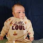 Emmie is registered to the contest to win money with this photo: baby, infant, child, face, clothing, sleeve, hand, cushion, fabric, text, pattern, mushroom, sitting, portrait, cute, young, indoors, expression, person, cozy