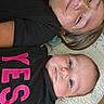 Emmie is registered to the contest to win money with this photo: child, baby, sibling, smile, face, portrait, lying_down, quilt, clothing, black_shirt, text_on_clothing, happy, young, cute, indoor, head, skin, eyes, hair, person
