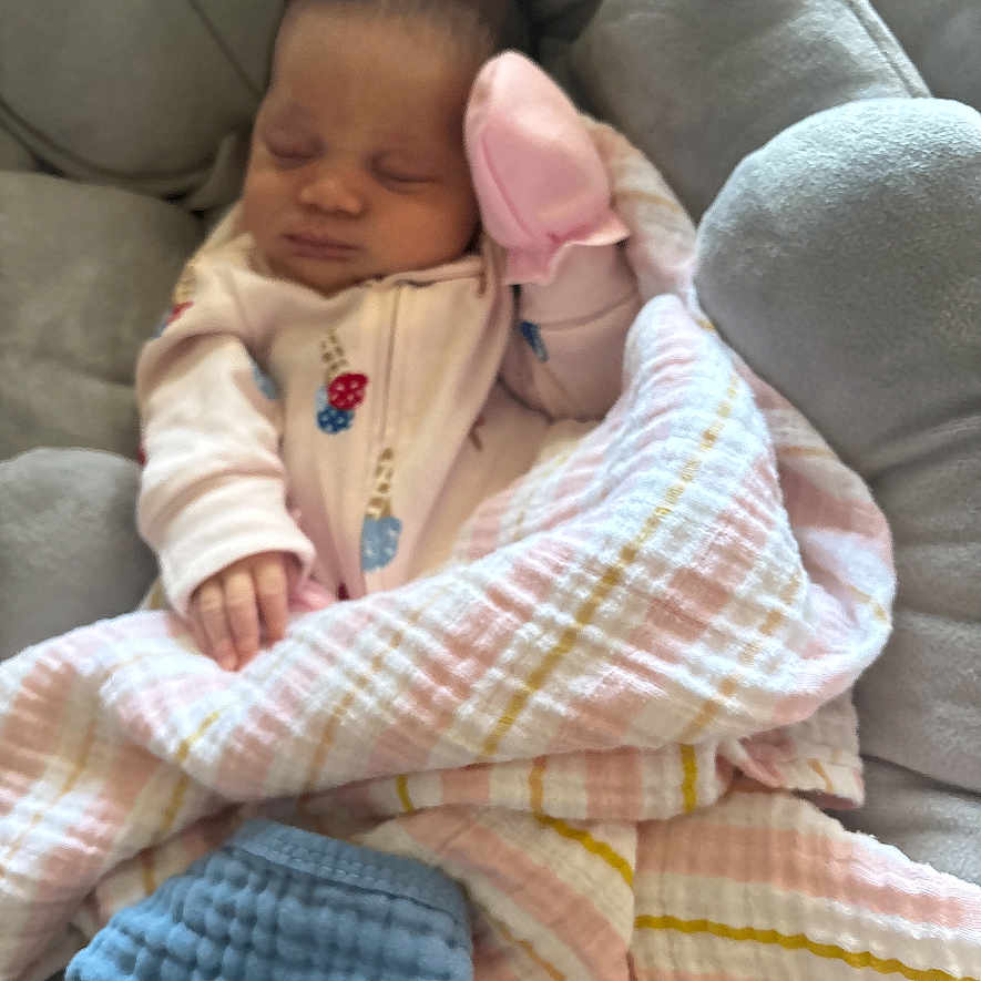 Camryn is registered to the contest to win money with this photo: baby, infant, sleeping, blanket, pink_mitten, cushion, soft_toy, cozy, resting, child, cute, indoors, wearing_pajamas, peaceful, newborn, portrait, comfort, relaxing, small_hands, nursery