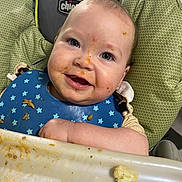 Moraya joined the competition — help win amazing prizes! baby, messy_face, high_chair, blue_bib, food, eating, smiling, happy, face, child, indoor, feeding, infant, plate, table, clothing, person, cute, dining, meal