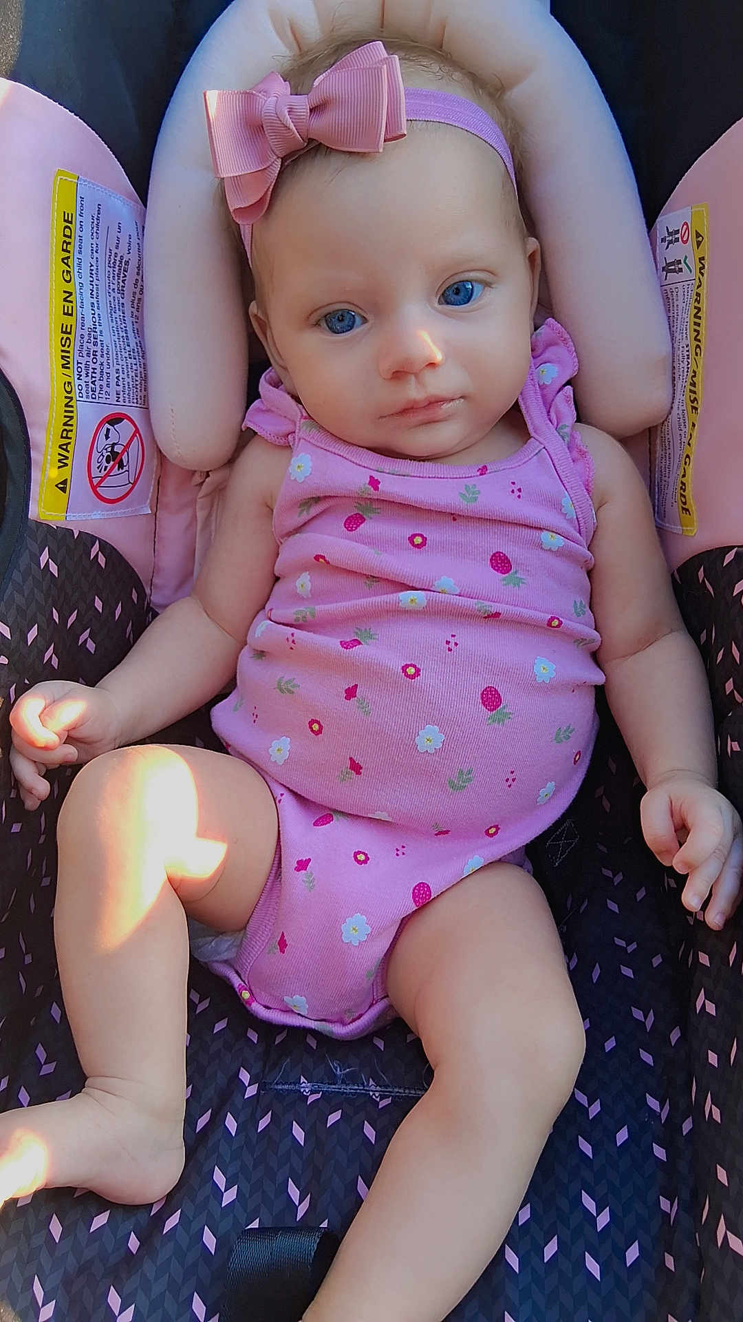 Remington is registered to the contest to win money with this photo: baby, infant, child, car_seat, pink_clothing, headband, bow, blue_eyes, onesie, warning_label, sitting, cute, soft_light, indoors, comfortable, portrait, skin, hand, foot, relax