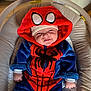 baby, child, infant, costume, spiderman, hood, smile, face, couch, furniture, indoor, cute, plush, clothing, person, seat, baby_rocker, happy, headwear, cute_face